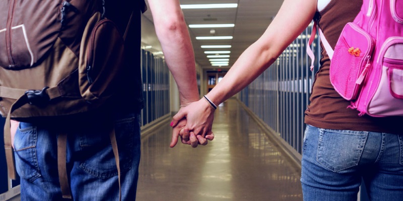 close up of high school couple holding hands in hallway